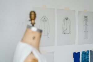 Blurred dummy placed near wall with various drafts of stylish clothes and samples of colorful textile in light modern atelier